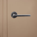 Lavuzo Caserta deurklink Gun Metal PVD gecoat op rond rozet gemonteerd op beige deur, vooraanzicht