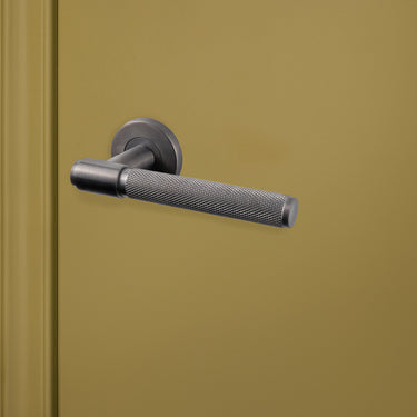 Cosenza Knurled PVD gecoate deurkruk Gunmetal met rond rozet op groene deur, rechteraanzicht