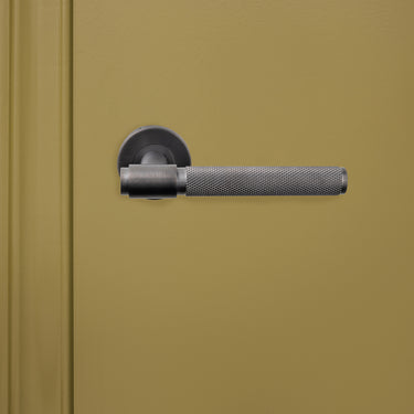 Lavuzo Cosenza gekartelde deurklink Gun Metal PVD op rond rozet gemonteerd op groene binnendeur, vooraanzicht