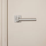 RVS binnendeurbeslag Lavuzo Grosetto op vierkant rozet op crèmekleurige deur, vooraanzicht