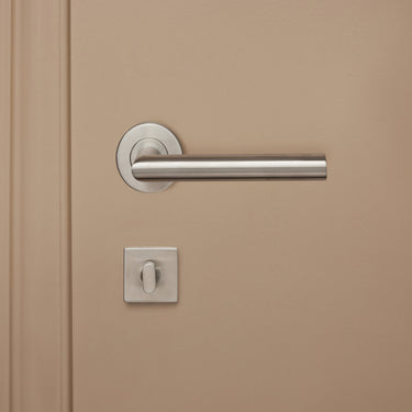 Modern RVS WC-beslag binnenzijde met draaiknop op vierkant rozet op beige binnendeur, vooraanzicht