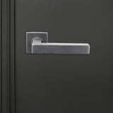 Viterbo PVD gecoate binnendeurkruk Gun Metal met vierkant rozet op donkere deur, vooraanzicht