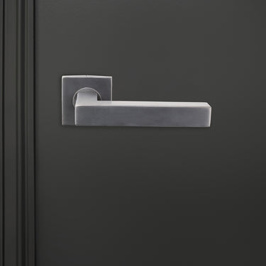 Viterbo PVD gecoate binnendeurkruk Gun Metal met vierkant rozet op donkere deur, vooraanzicht